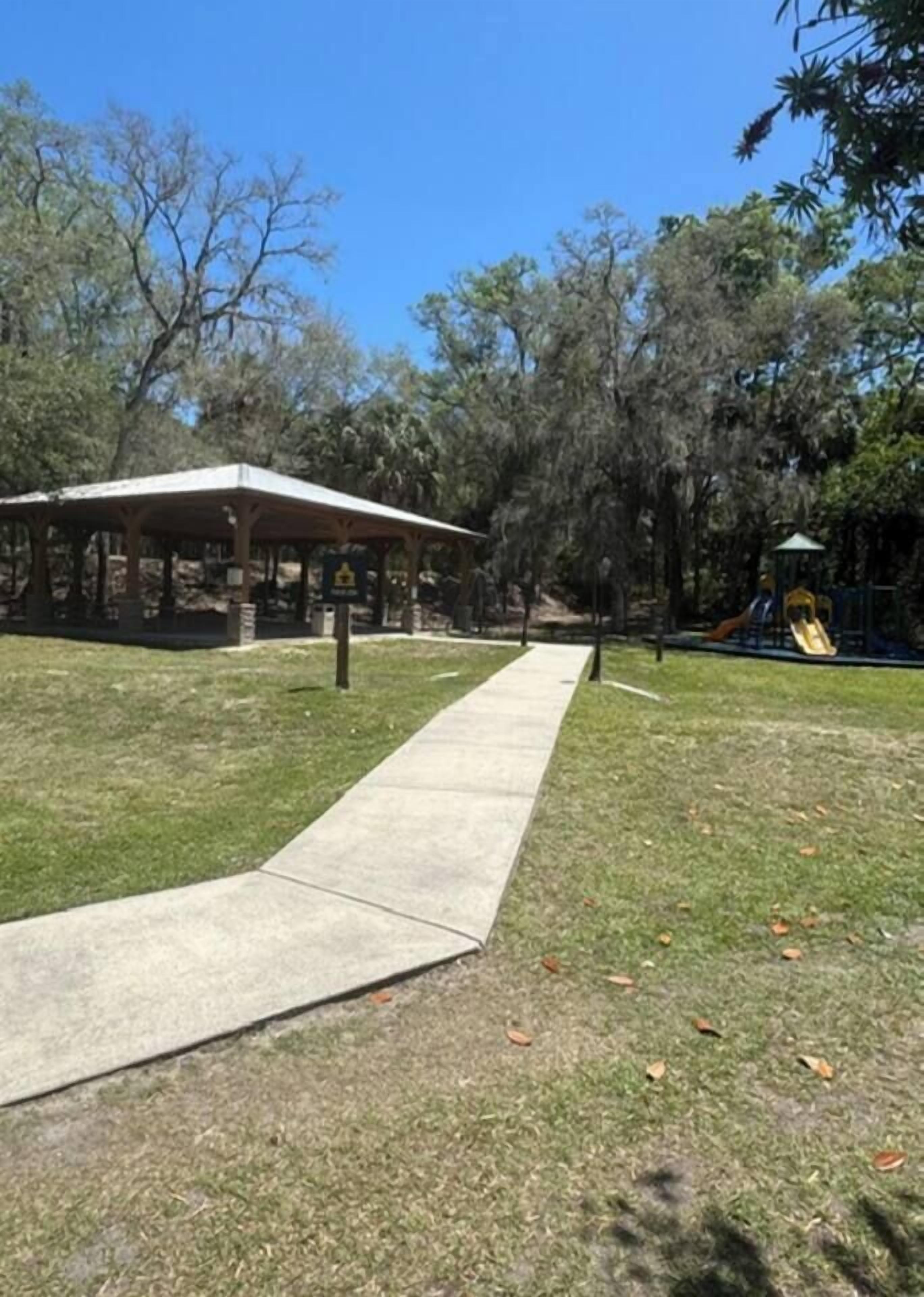 Un parque con un sendero pavimentado, un pabellón techado y juegos infantiles.