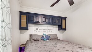 Ein Schlafzimmer mit einem Bett, einem Kopfende mit eingebauten Schränken und einem an der Wand befestigten Schild.