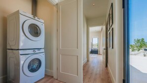 Een wasserette met gestapelde wasmachines en drogers, een gang naar een slaapkamer en uitzicht door een glazen deur.