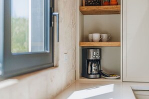 Eine Küchenzeile mit einer Kaffeemaschine, einem Regal mit Tassen und einem Fenster.