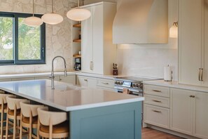 Eine moderne Küche mit einer zentralen Kochinsel, Barhocker, einem Einbauofen und einer Wand mit Steinakzenten.