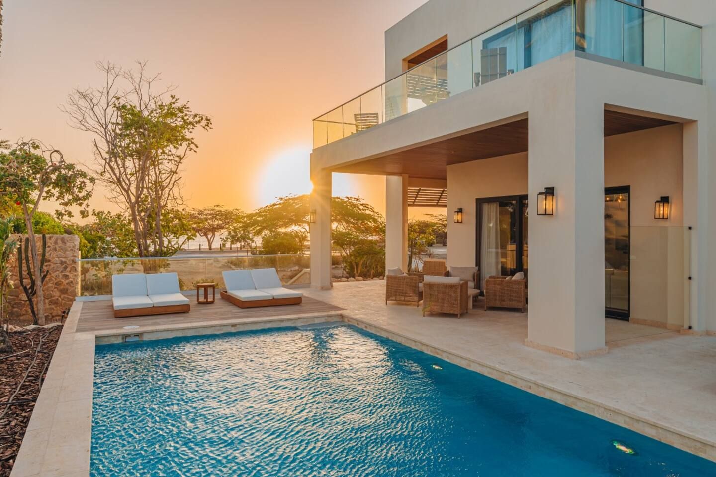 A modern outdoor pool area with lounge chairs and a covered seating area, surrounded by natural vegetation.