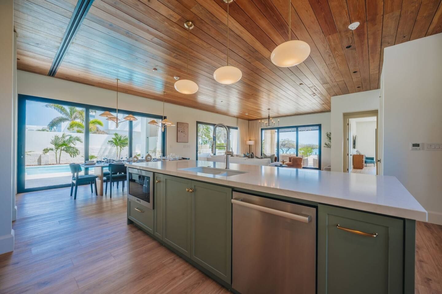 Een moderne keuken met een groot eiland, houten plafond en grote ramen met uitzicht op een zwembad.