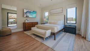 Een slaapkamer met een bed, een nachtkastje, een bankje, een groot raam en een schilderij aan de muur.
