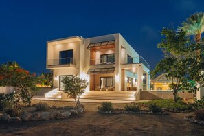 Ein modernes, zweistöckiges Haus mit Balkon, überdachter Außenlounge und gepflegtem Garten.