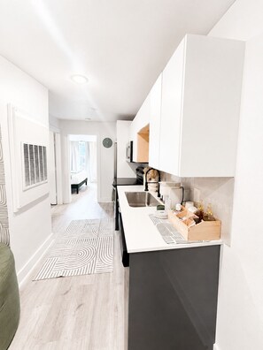 Eine moderne Küche mit weißen Schränken, einer zentralen Kochinsel mit Spüle und Blick in den angrenzenden Wohnbereich.