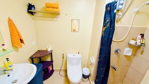 Een badkamer met toilet, wastafel en douche. Handdoeken en toiletartikelen hangen aan de muur.