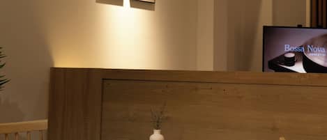 A dining area with a wooden table, chairs, a hanging paper lantern, framed pictures on the wall, and a television displaying 'Bossa Nova'.