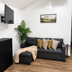 A modern living room with a dark grey sofa, a beige throw blanket, and a potted plant. - Luxury Cozy  1-bedroom house in Quitman with AC (Quitman)