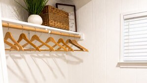 Ein heller Raum mit einem Holzständchen für Kleidung, einem weißen Stuhl und einem Fenster mit Jalousien.