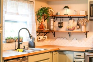Eine Küche mit Spüle, einer Holz Arbeitsplatte, hängenden Regalen mit Küchenutensilien und einem Topf mit Pflanze.