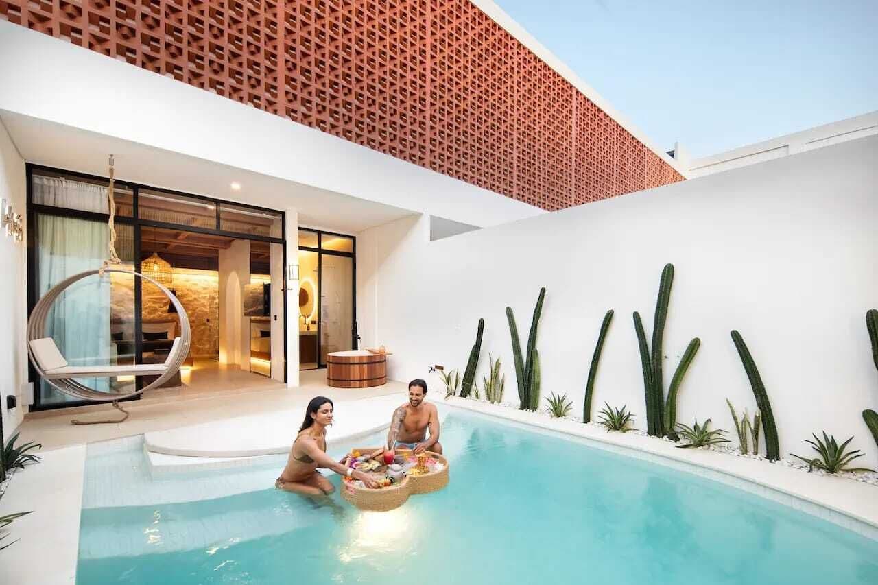 A modern pool area with a glass-enclosed lounge, a brick wall, and cacti along the poolside.