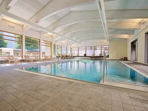 Ein Innenpool mit gefliestem Boden, Liegestühlen und großen Fenstern.