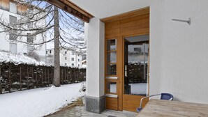 Una puerta de madera con paneles de vidrio, una silla de metal y una zona de entrada con pavimento de piedra.