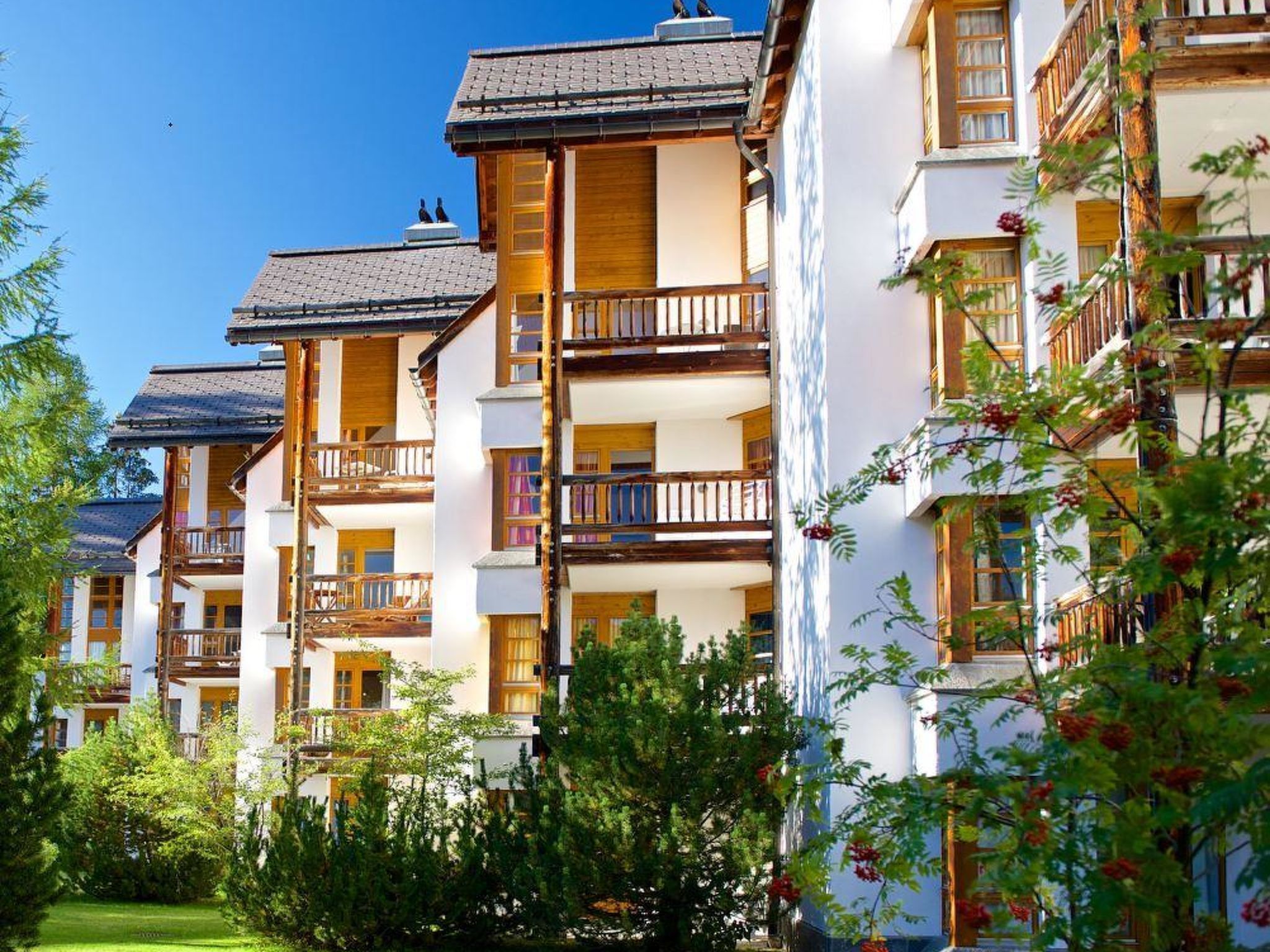 A row of traditional chalet-style buildings with wooden balconies and a well-maintained garden in front.