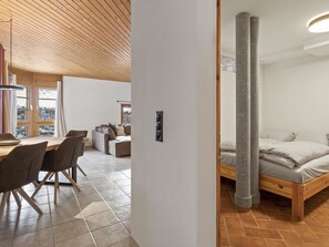 Ein modernes Interieur mit Holzboden, einem Essbereich mit Stühlen und Tisch sowie einem Schlafzimmer mit Bett und zwei Säulen.