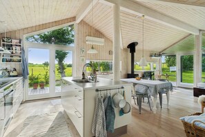 A spacious kitchen with large windows, a central island, and a dining area with a view of the outdoors. - Lovely holiday home with great view (Græsted)
