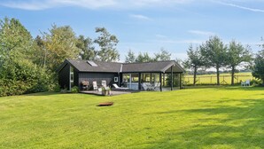 A modern house with a covered patio, a lawn, and trees in the background. - Lovely holiday home with great view (Græsted)