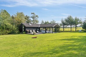 Ein modernes Haus mit überdachter Terrasse, Rasen und Bäumen im Hintergrund.