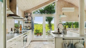 A modern kitchen with a large window, stainless steel appliances, and a view of a green landscape. - Lovely holiday home with great view (Græsted)
