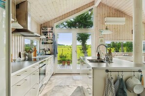 Eine moderne Küche mit einem großen Fenster, Edelstahlgeräten und Blick auf eine grüne Landschaft.