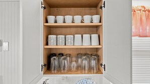 A kitchen cabinet with white mugs, patterned mugs, and glass jars. - Cherry Grove Coastal Escape · 2BR · Steps to Beach (North Myrtle Beach)