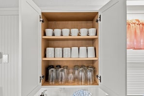 A kitchen cabinet with white mugs, patterned mugs, and glass jars.