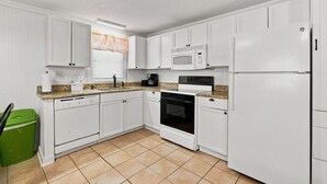 A kitchen with white cabinets, a microwave, a stove, and a refrigerator. - Cherry Grove Coastal Escape · 2BR · Steps to Beach (North Myrtle Beach)