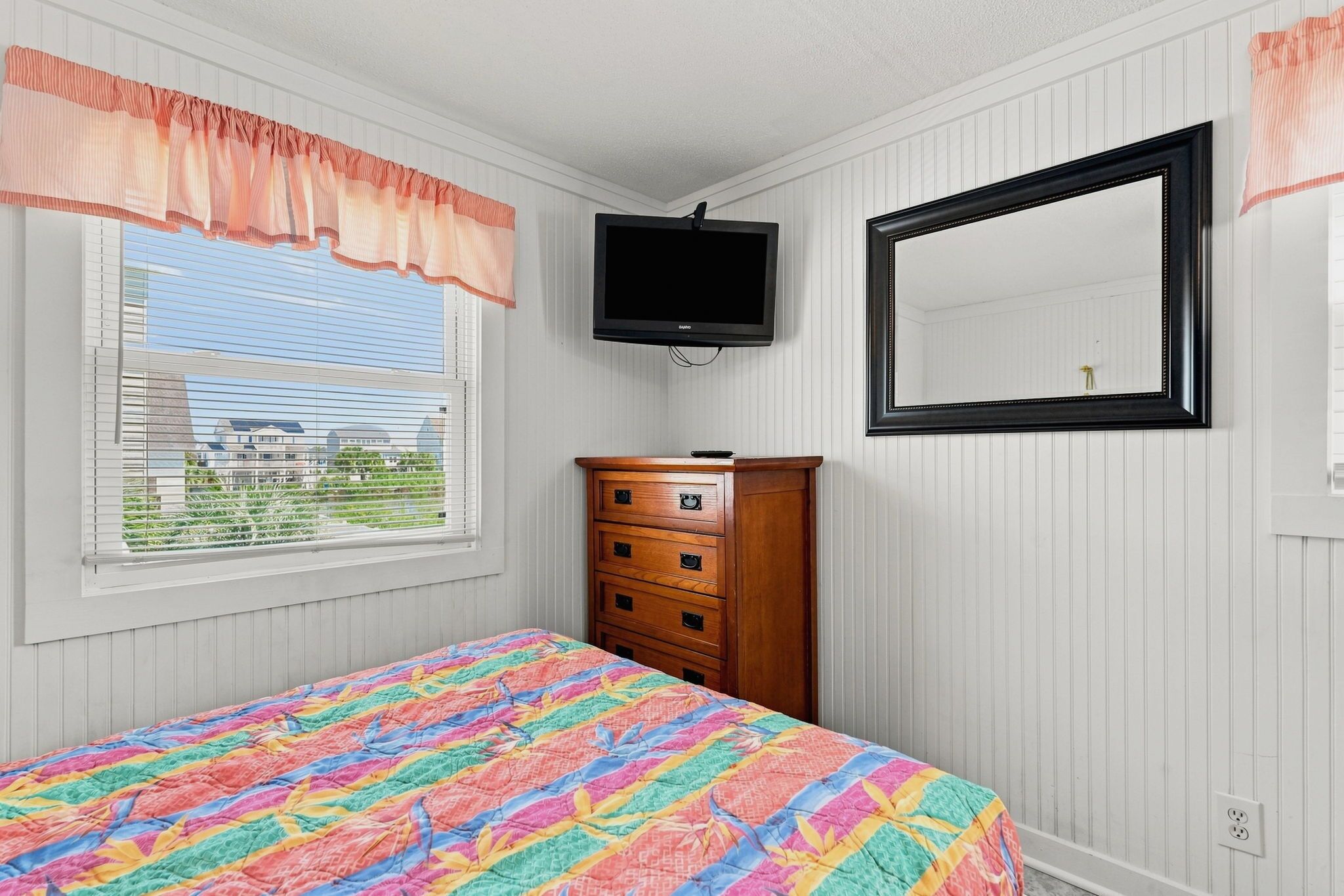 A bedroom with a bed, a dresser, a television, and a mirror.