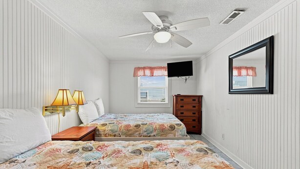 A bedroom with two beds, a ceiling fan, a TV, and a dresser. - Cherry Grove Coastal Escape · 2BR · Steps to Beach (North Myrtle Beach)