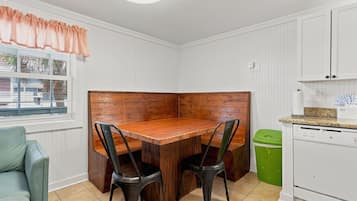 A compact kitchen with a wooden dining table, two chairs, a green trash bin, and white cabinetry.