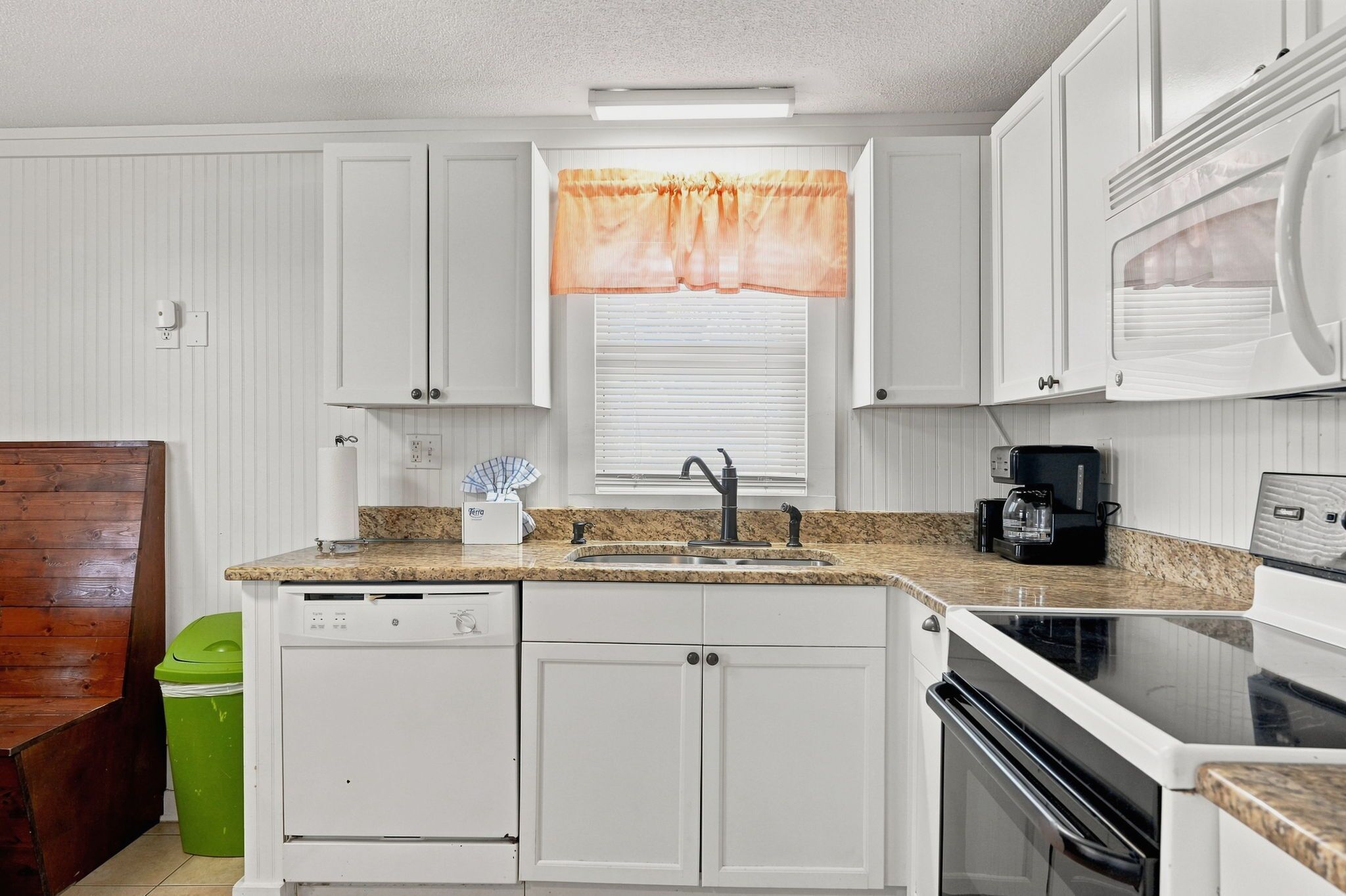 A kitchen with white cabinets, a granite countertop, a sink, a coffee maker, and a microwave.