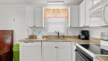 A kitchen with white cabinets, a granite countertop, a sink, a coffee maker, and a microwave.
