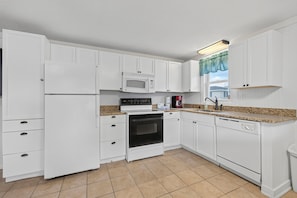 A kitchen with white cabinets, a microwave, an oven, a dishwasher, and a granite countertop.