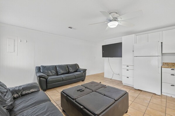 A room with a black leather sofa, a matching ottoman, a white wardrobe, and a ceiling fan.