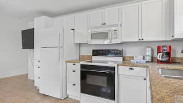 A kitchen with white cabinets, a microwave, a stove, and a coffee maker.