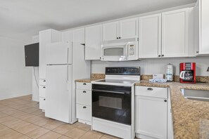 A kitchen with white cabinets, a microwave, a stove, and a coffee maker.