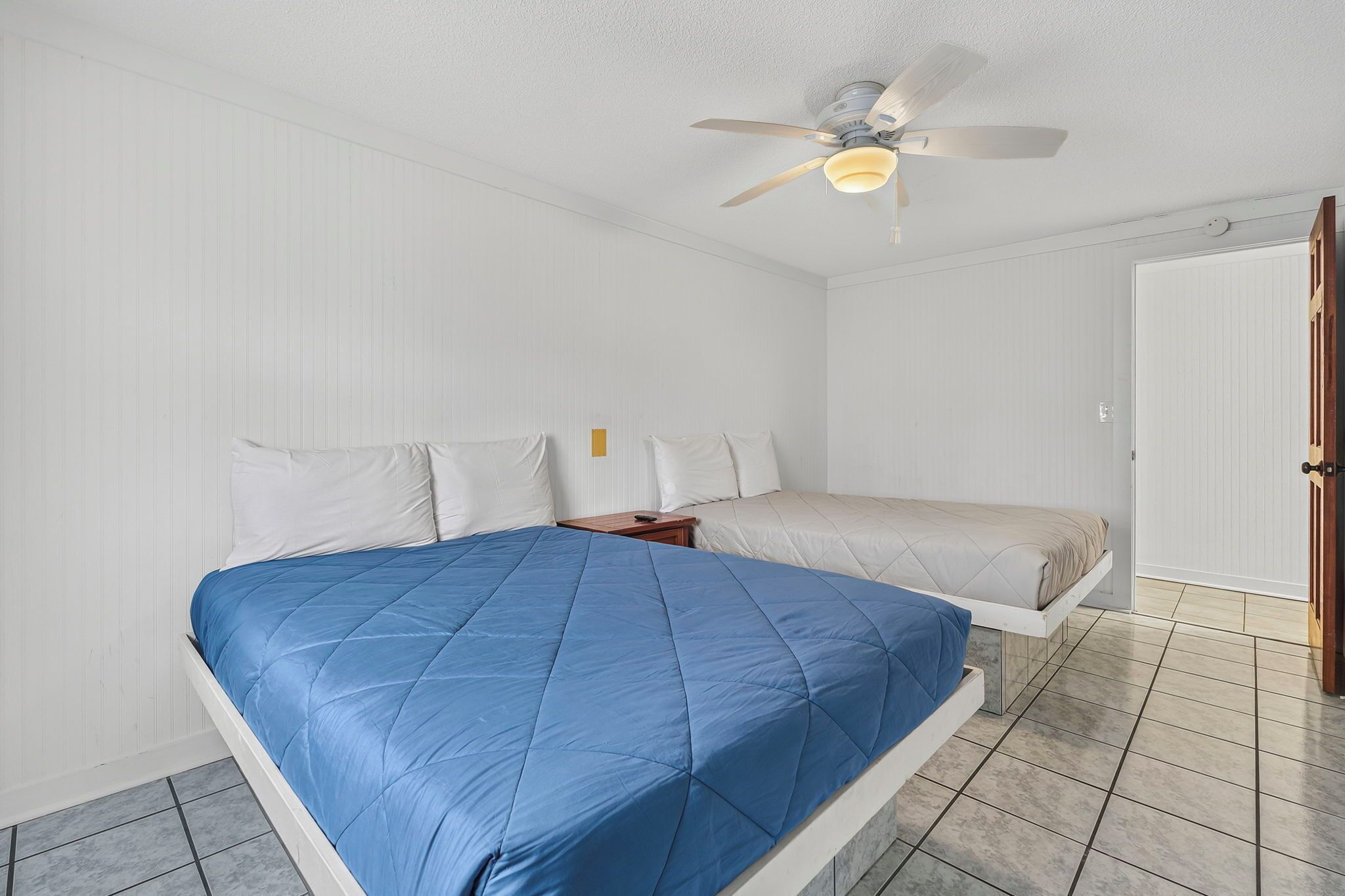 A bedroom with a bed, a nightstand, a ceiling fan, and a door.