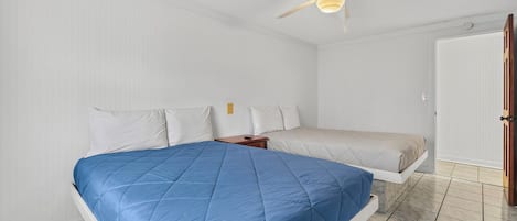 A bedroom with a bed, a nightstand, a ceiling fan, and a door.