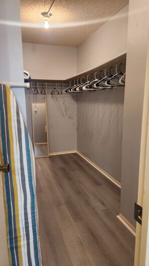 Un dressing accessible sans porte, doté d’un plancher en bois, d’un luminaire au plafond et d’une porte donnant sur une autre pièce.