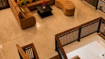 A spacious living area with a sectional sofa, ottoman, and coffee table, a staircase with wooden railings, and a view of the outside through large windows.