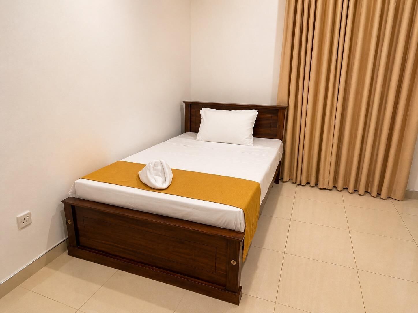 A single bed with a wooden frame, white bedding, and a yellow accent on the bedspread.