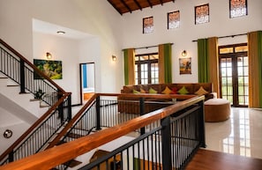 Un vaste espace de vie agrémenté d’un escalier en bois, d’un canapé avec des coussins colorés et d’une grande fenêtre ornée de rideaux verts.