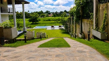 A stone pathway leading to a pool area with a view of a lush green landscape and a house with a balcony.