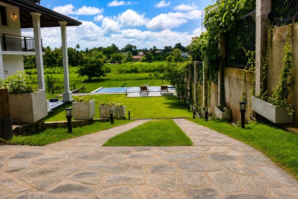 A stone pathway leading to a pool area with a view of a lush green landscape and a house with a balcony.