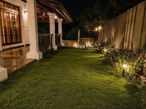 A well-lit outdoor area with a lawn, a wooden fence, and a building with a porch.