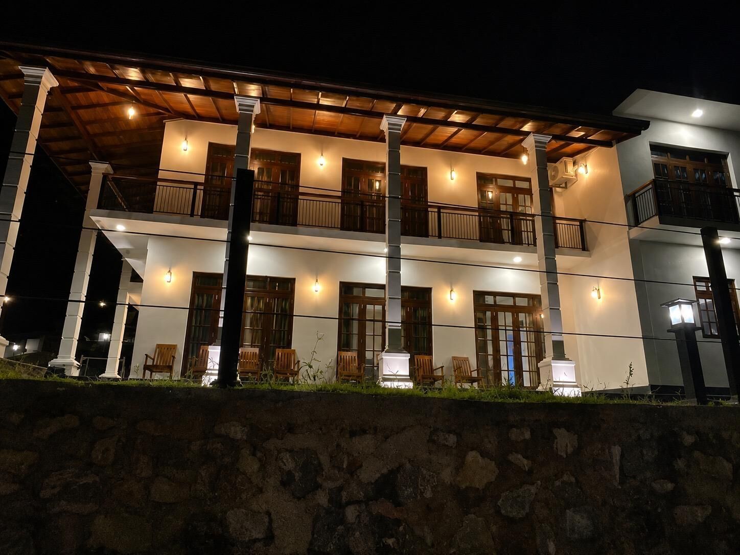 A multi-story building with balconies, outdoor seating, and a stone wall in the foreground.