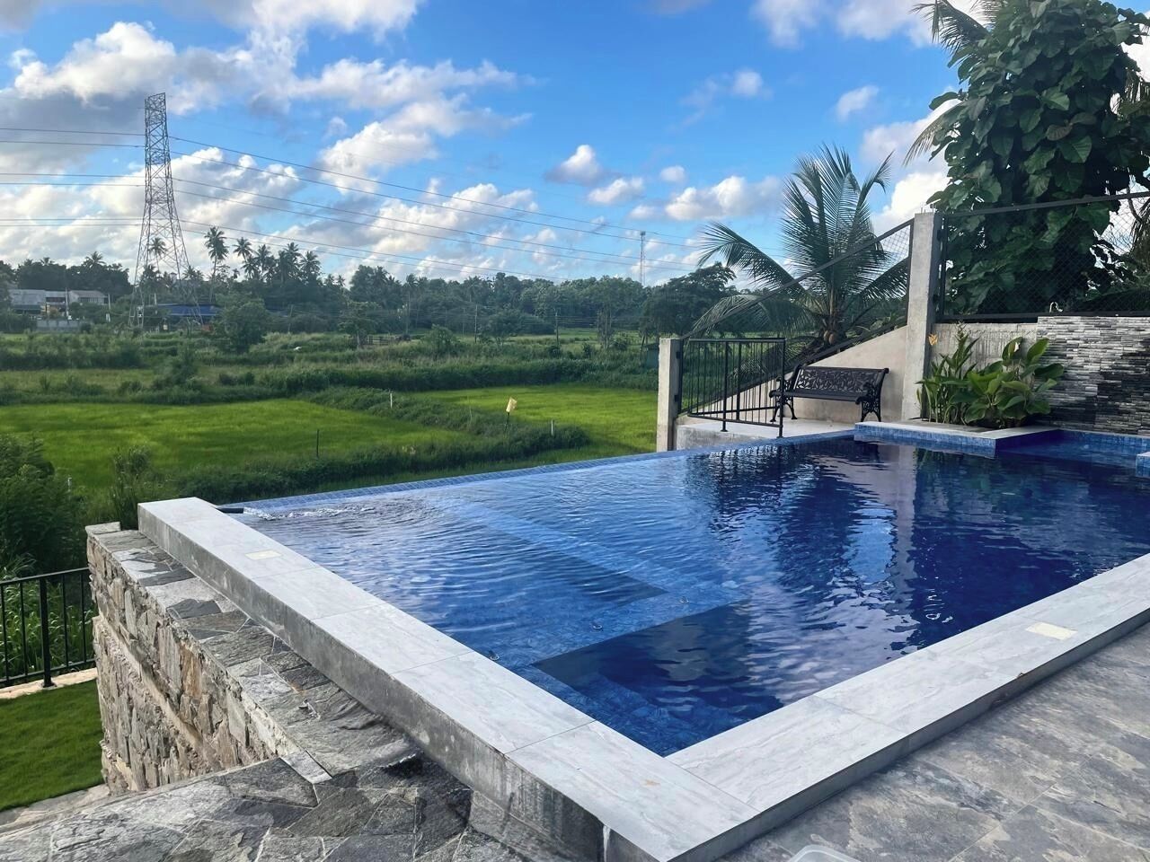 A swimming pool with a stone edge, surrounded by a stone wall and a metal fence.