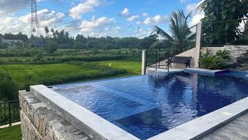 A swimming pool with a stone edge, surrounded by a stone wall and a metal fence.