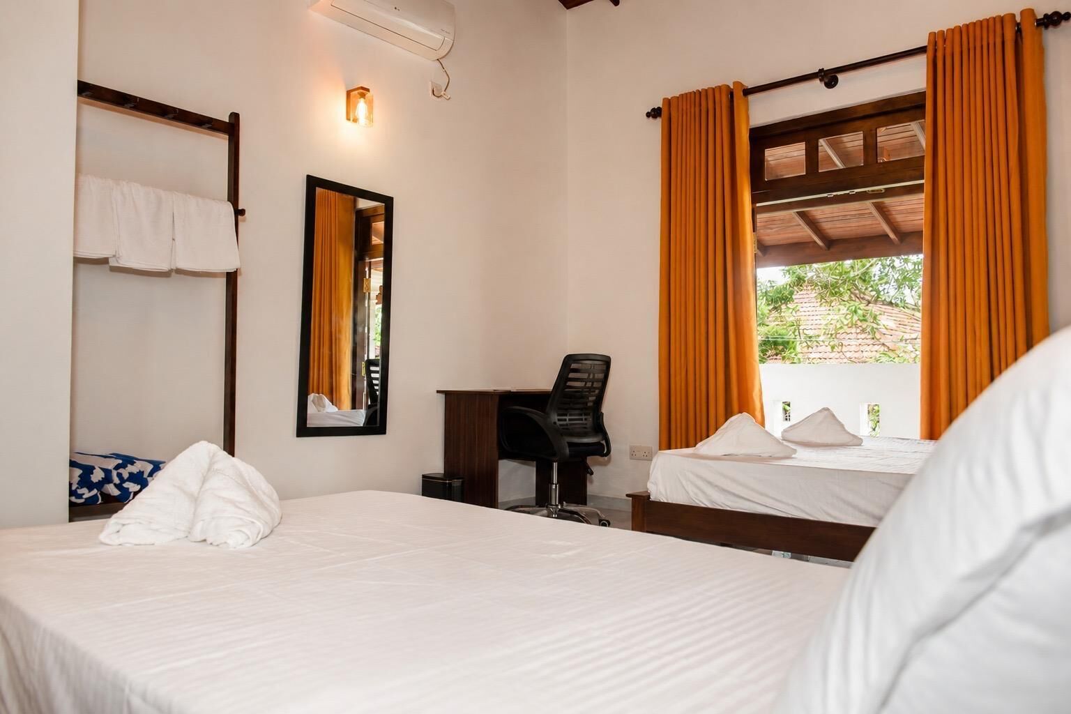 A hotel room with a bed, a desk, a chair, a mirror, and a window with curtains.